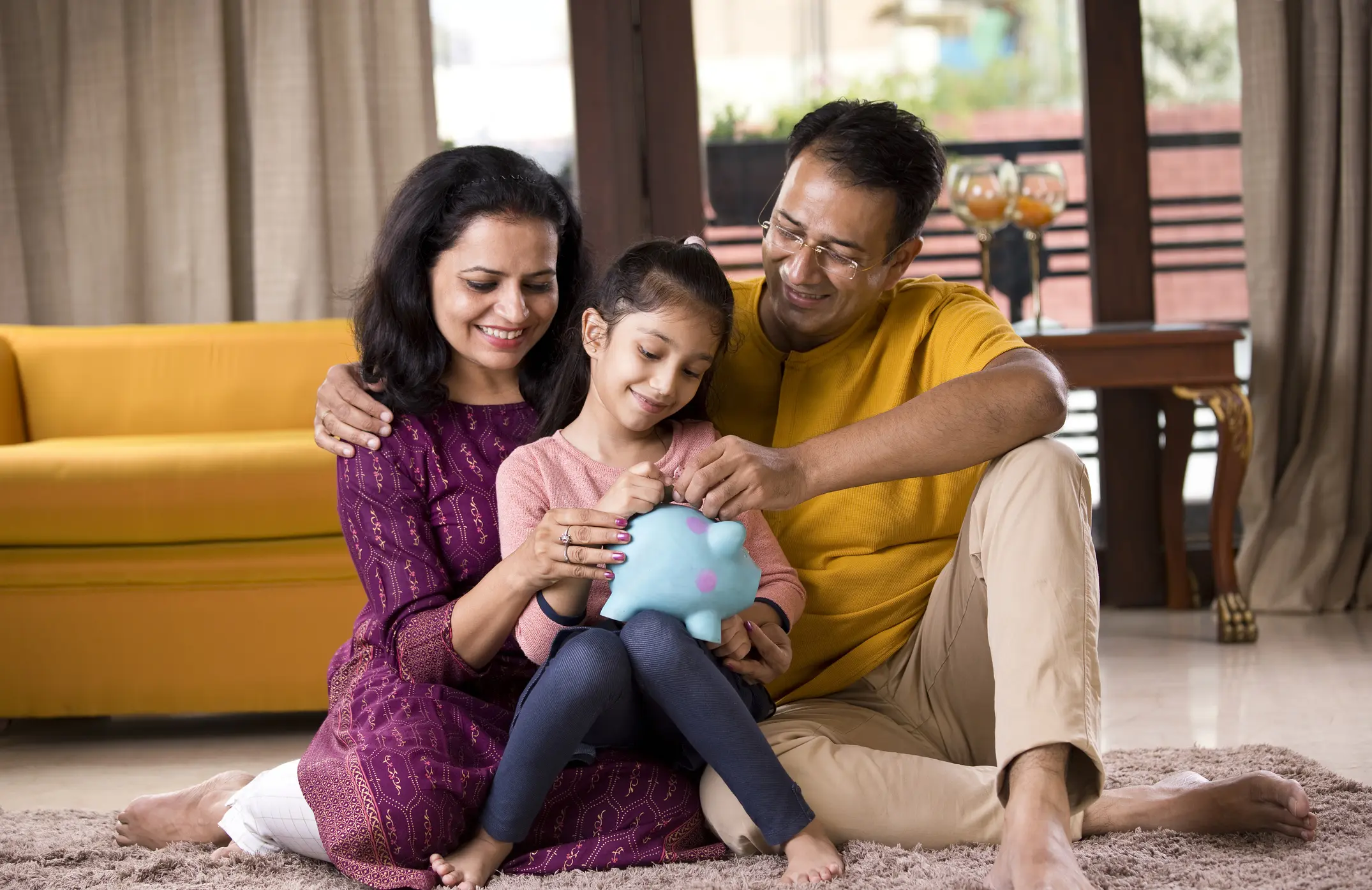 Happy parents with child inserting coin into piggy bank